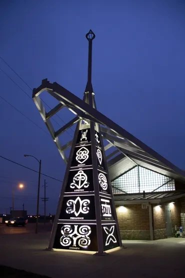 Adinkra Tower lit at dusk at the Riverview MetroBus Center, its panels cut with Adinkra symbols
